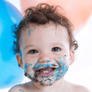 A baby smiling into the camera with frosting all over his face