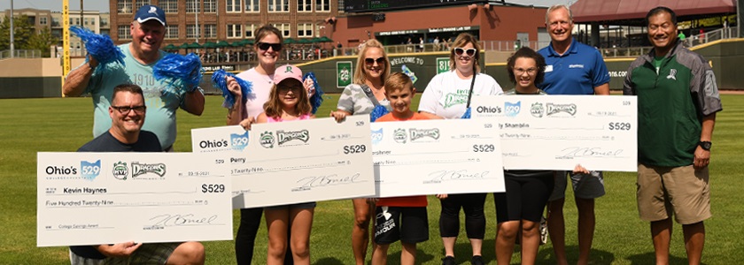 Families standing on baseball field with oversized checks