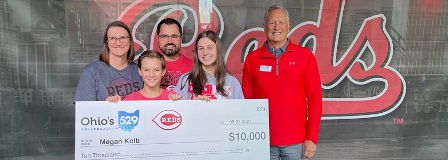 Family holding oversized check in front of Cincinnati Reds signage