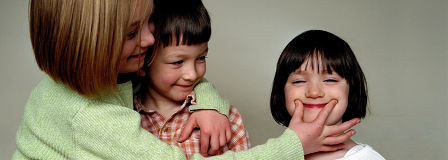 An older sister and younger brother make their sister smile
