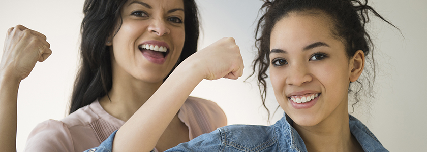 Mother and teenage daughter flex and smile at the camera