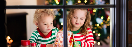 Toddler and older sister admire gingerbread house