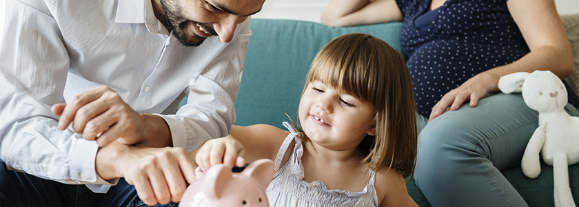 Small Changes Can Make a Big Impact Dad helps young daughter place some coins in her piggy bank as pregnant mom watched from the couch.
