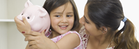 Mom smiling at daughter who is shaking a pink piggy bank