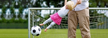 Dad swinging daughter around to try to kick soccer ball