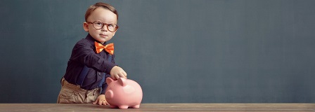 Little boy with bow tie placing coins in a piggy bank