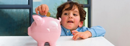 Little boy stretching to place coins in a piggy bank
