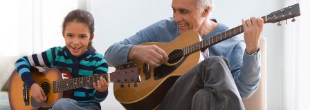 Grandfather teaching his granddaughter how to play the guitar