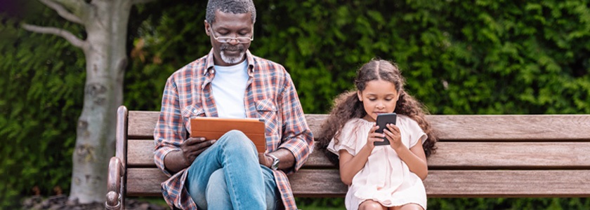 Learn More About 529 Holiday Gift Giving With Dec. 14 Webinar Grandfather and granddaughter looking at electronics while sitting on park bench wh
