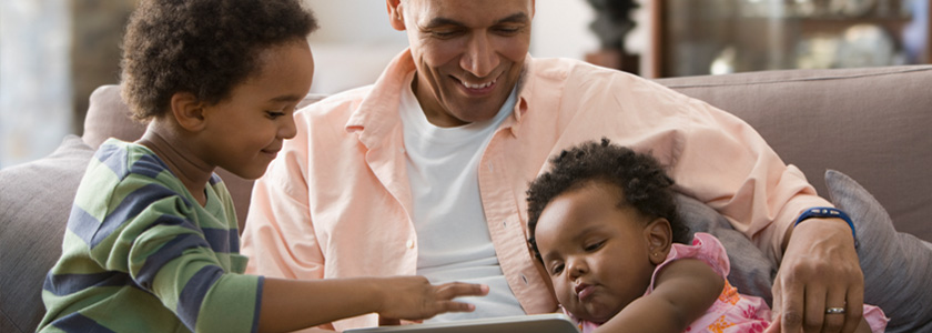 Grandfather reading book with grandson while holding grandbaby