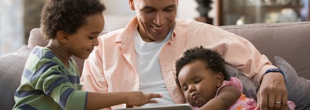 Grandfather reading book with grandson while holding grandbaby