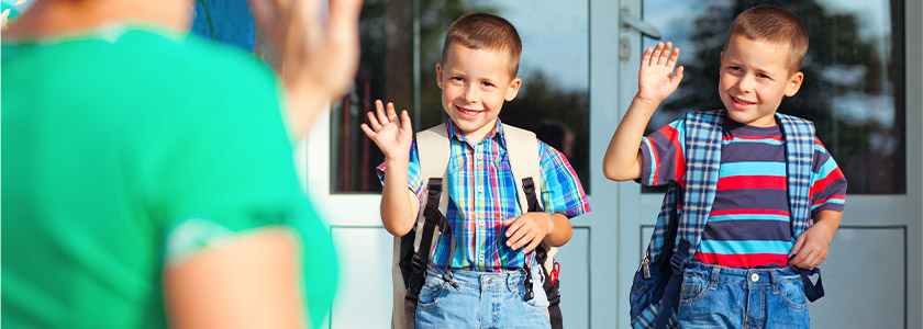 Twin boys waving goodbye to their Mom in front of school entrance