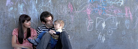 Mother, father, and son sit together while leaning on a wall with chalk art