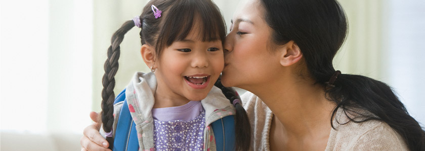 Mother kisses daughter as she gets ready to leave the house for school