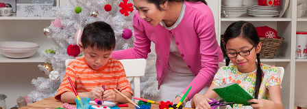 Two children creating holiday ornaments while mom watches