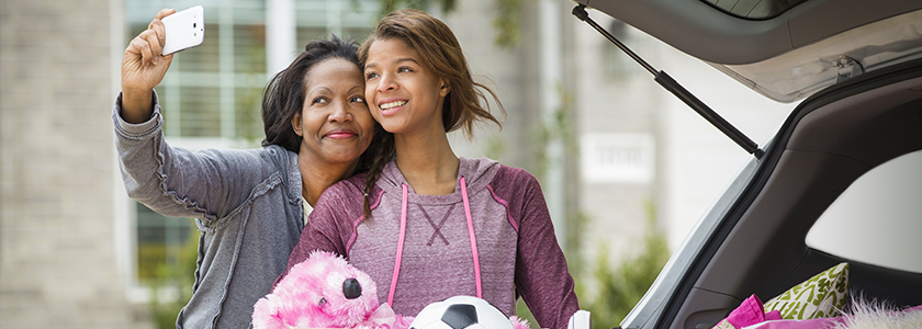 Mother taking a picture with her daughter as they unload the car at college drop-off.