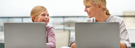 Mom and daughter smile at each other while working on their laptops