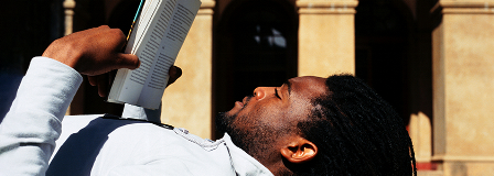 Man reading a book while lying on the the ground in front of college building