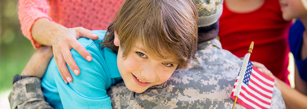 Little boy holding an American flag hugs a man in a military uniform