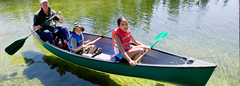 Father, son, and daughter sit in canoe, with fishing poles, on a crystal clear lake