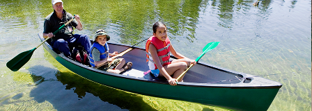 Father, son, and daughter sit in canoe, with fishing poles, on a crystal clear lake