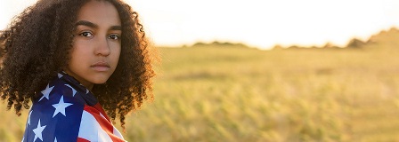 Young woman standing in a field with the flag wrapped around her shoulders