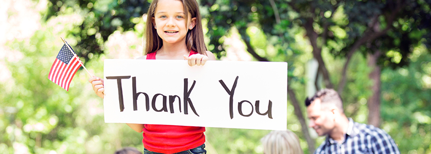 Young girls holding a sign with "thank you" written on it and an American flag