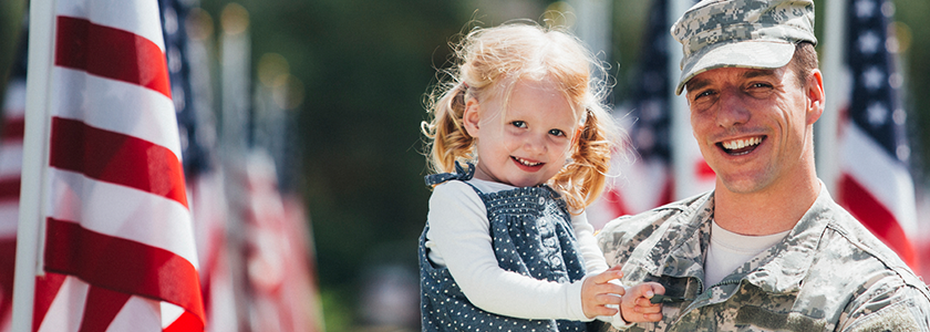 Smiling military father holds his daughter in field of American flags