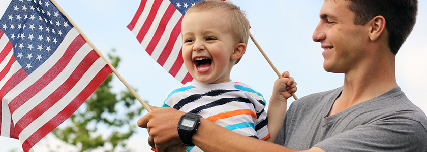 HOLIDAY_002 Father smiling at laughing son while they hold small American flags