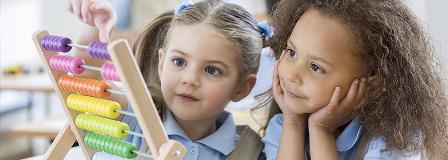 Two young girls in school uniforms play with an abacus or counting frame