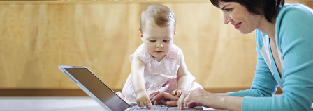 Mom smiling at baby playing with laptop keyboard