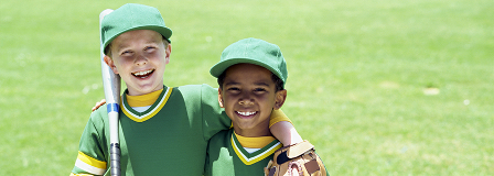 Two young boys in green baseball uniforms smiling at the camera
