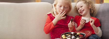 Two sisters eating chocolates from a heart-shaped box