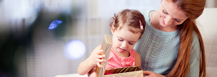 Mother holds daughter as she opens a gift box