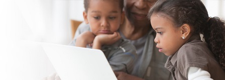 Two children look at laptop with grandfather